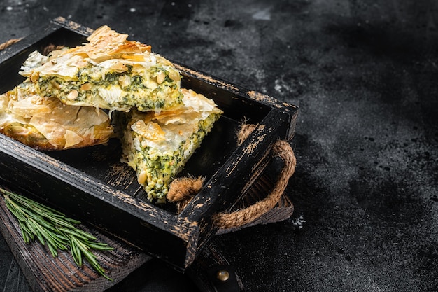 Trozos de pastel de espinacas, pastel griego Spanakopita en bandeja de madera. Fondo negro. Vista superior. Copie el espacio.