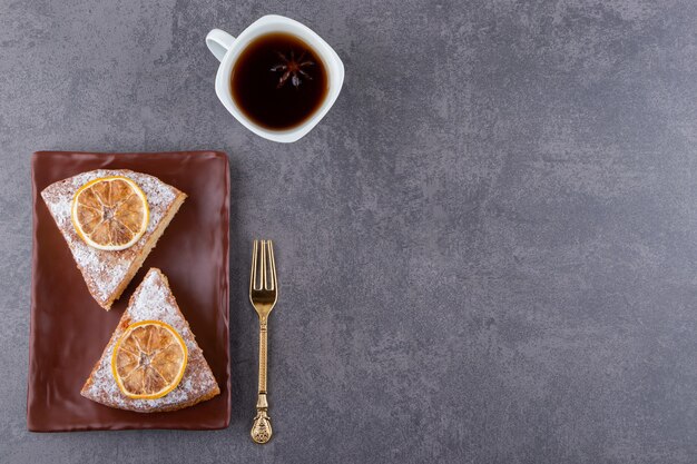 Trozos de pastel con tenedor y taza de té negro colocados sobre la mesa de piedra.