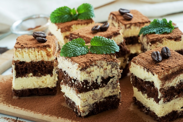 Trozos de pastel de tiramisú con crema delicada, granos de café y hojas de menta.