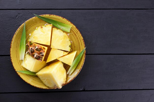 Trozos de piña en plato amarillo Fruta de piña con hojas verdes sobre fondo oscuro Vista superior Espacio de copia