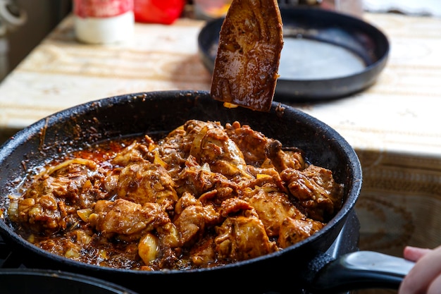 Trozos de pollo fritos en salsa de especias en una sartén profunda con una espátula de madera