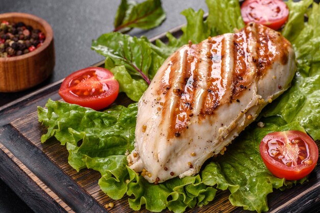 Trozos de pollo, tomates y hojas de lechuga sobre un fondo de hormigón oscuro. Deliciosa comida sana