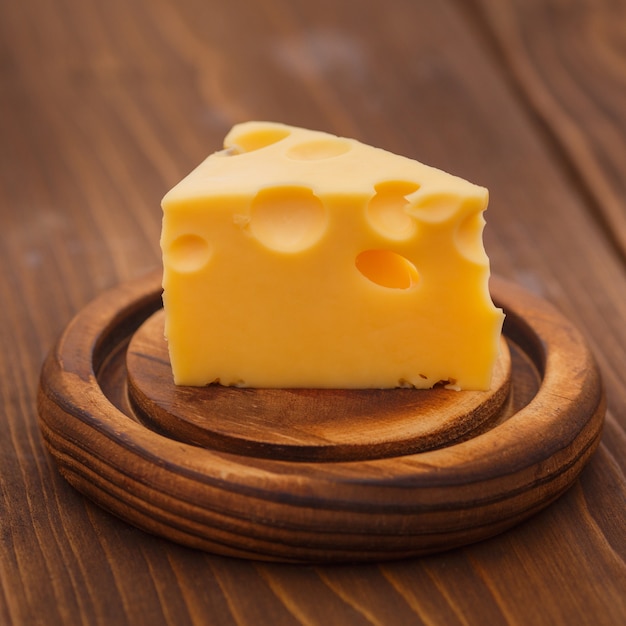 Trozos de queso sabroso con grandes agujeros en el tablón de madera.