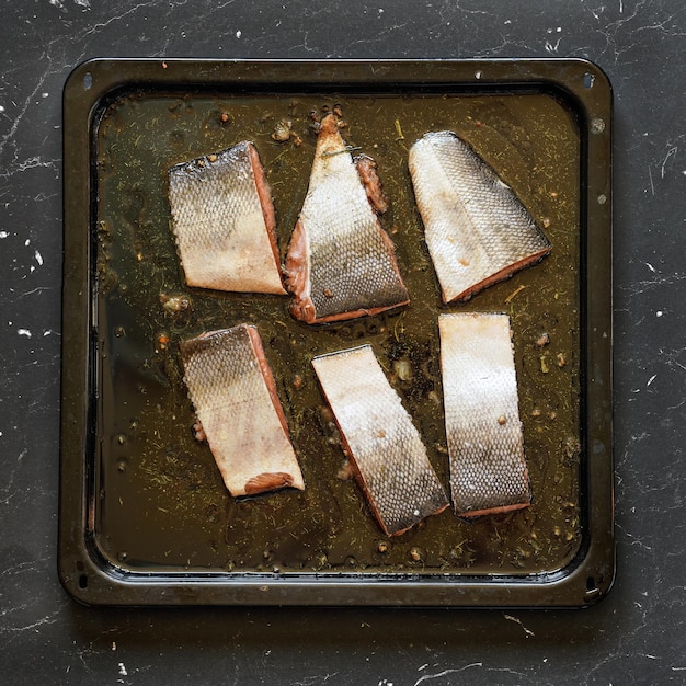 Trozos de salmón con piel en aceite de cocina y algunas hierbas en sartén - para hornear