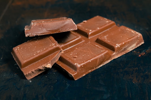 Trozos de tableta de chocolate negro sobre una superficie oscura e industrial.