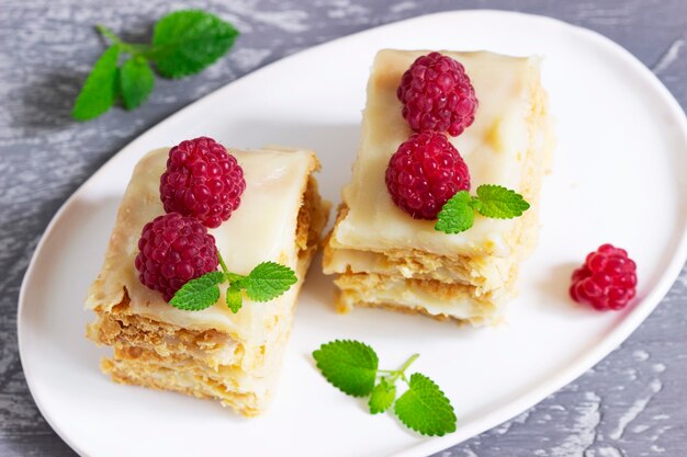 Trozos de tarta de Napoleón decorados con frambuesas y hojas de bálsamo de limón sobre un fondo claro.