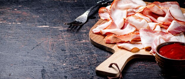 Foto trozos de tocino en una tabla para cortar con salsa de tomate