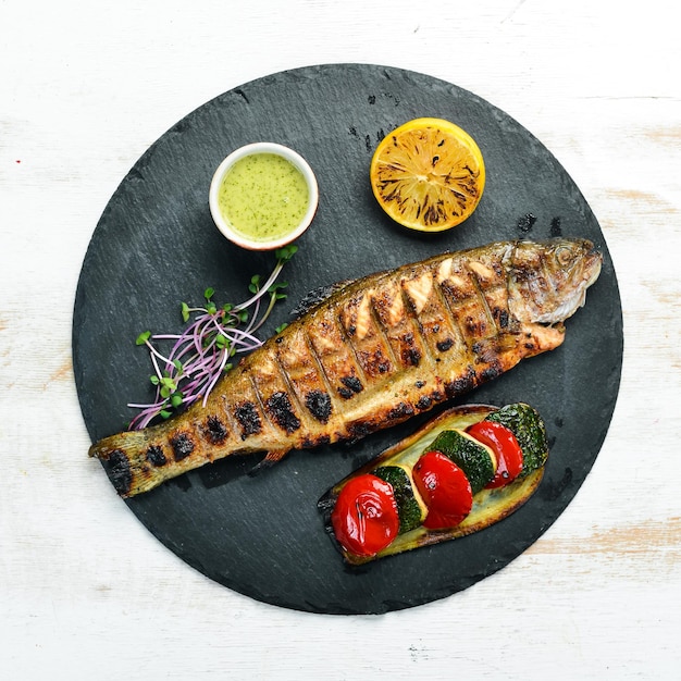 Trucha a la parrilla con verduras en un plato negro. Vista superior. espacio libre para su texto. Estilo rústico.