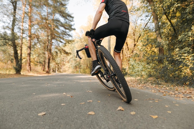 Trucos ciclistas en bicicleta en la carretera en la foto del bosque de otoño detrás del foco en la rueda