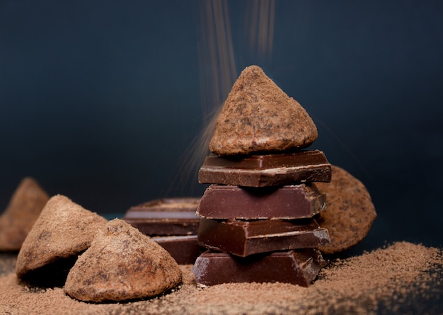 Trufa de chocolate e pedaços de chocolate e cacau em pó voando sobre um fundo escuro