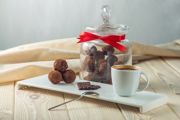 Trufas de bolas de chocolate en un platillo junto a una jarra de dulces y una taza de café. El concepto de regalos deliciosos postres