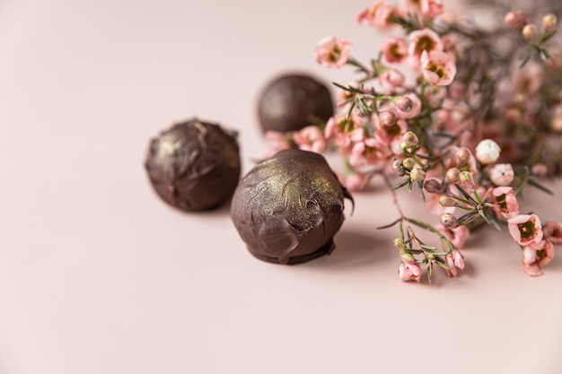 Trufas de chocolate sobre fondo rosa decorado con flores rosas. Minimalismo. Enfoque selectivo.