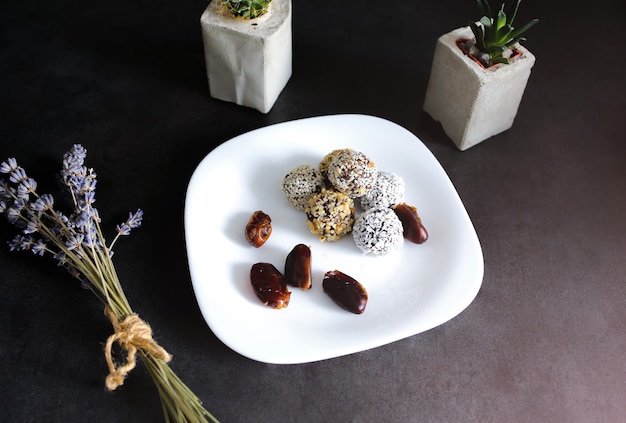 Trufas crudas caseras con cacao, nueces, coco y dátiles en plato blanco y mesa gris. Lavanda y suculentas en jarrones de hormigón en el fondo. Caramelos veganos, orgánicos y saludables.