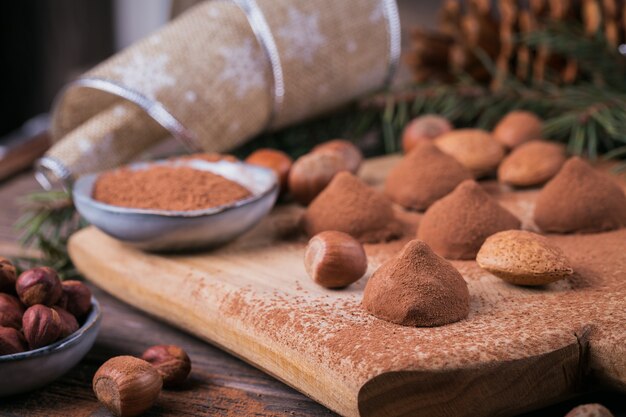 Trufas de chocolate caseiras, nozes, amêndoas e cacau em pó na tábua de madeira. decoração do feriado de inverno.