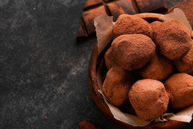 Trufas de chocolate com cacau em pó em prato de madeira no antigo fundo de mesa de concreto escuro Saborosas trufas de chocolate doce doces Dia dos namorados e conceito de dia das mães com espaço de cópia Vista superior