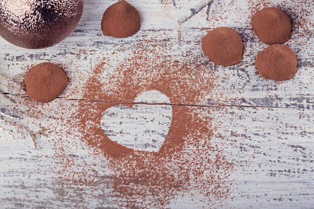 Trufas de chocolate escuro caseiro com pó de cacau em forma de coração e decoração de inverno na mesa de madeira rústica branca. Fundo de férias de inverno. Vista superior com espaço para texto.