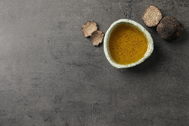 Trufas frescas y aceite en un tazón sobre una mesa gris plana Espacio para texto