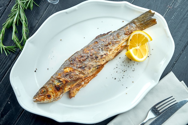 Truta grelhada inteira no fogo de carvão, servida em prato branco com limão sobre superfície de madeira escura.