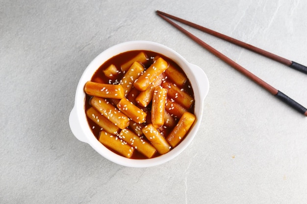 Tteokbokki com gergelim branco em tigela branca com fundo cinza