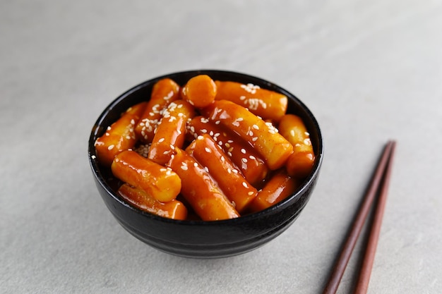 Tteokbokki mit weißem Sesam in weißer Schüssel mit grauem Hintergrund