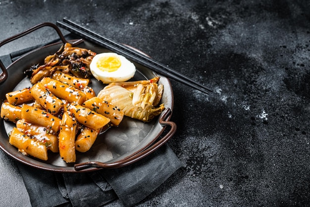 Tteokbokki Topokki Stick Reiskuchen in scharfer und würziger Sauce mit Ei und Pilzen Schwarzer Hintergrund Draufsicht Kopierbereich