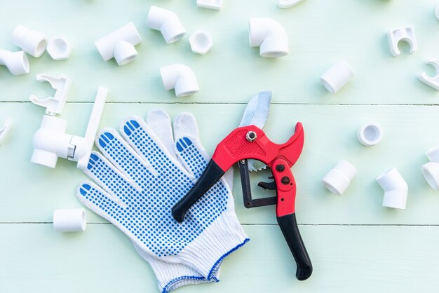 Tuberías y acoplamientos de polipropileno. Guantes y un cortatubos sobre una mesa azul.