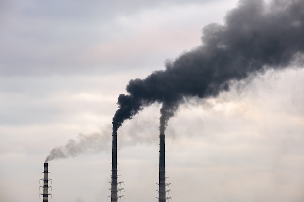Tuberías altas de la planta de energía de carbón con humo negro subiendo la atmósfera contaminante.