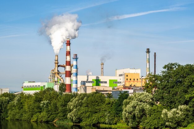 Tuberías del aserradero de la planta de la empresa de carpintería con un hermoso reflejo en el agua azul del río Concepto de contaminación del aire Paisaje industrial contaminación ambiental residuos de la planta de energía térmica