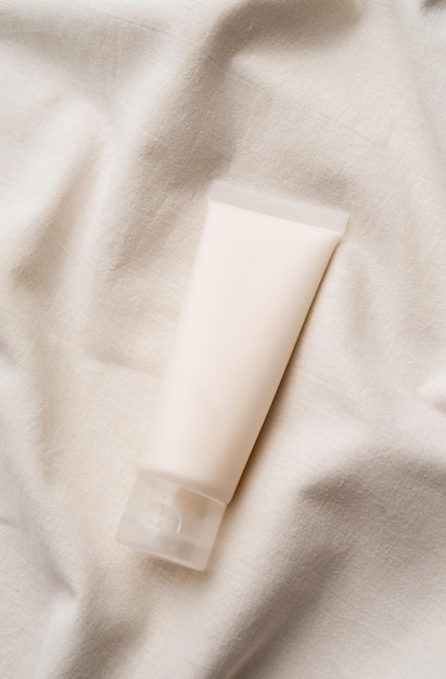 Tubo branco de produto de skincare facial de maquete de vista superior com rótulo em branco em fundo ondulado farbic