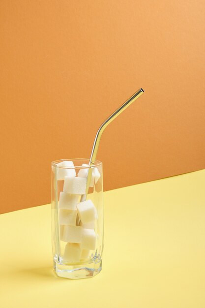 Tubo de cóctel y cubos de azúcar blanca en un vaso.