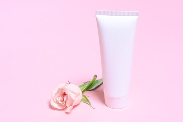 Tubo cosmético vacío blanco sobre un fondo rosa con delicadas rosas rosas