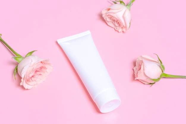 Tubo cosmético vazio branco sobre um fundo rosa com delicadas rosas cor de rosa