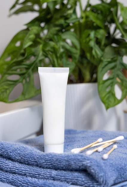 Foto tubo de crema blanca en toallas azules cerca del lavabo y monstera verde en la maqueta de la tapa del baño