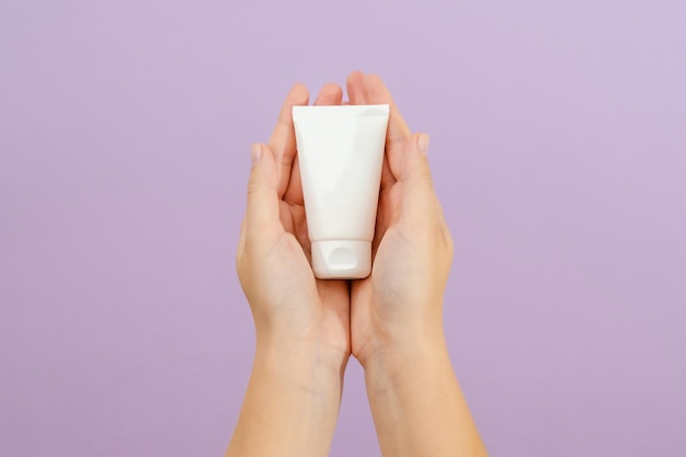 Tubo de crema cosmética en mano de mujer sobre fondo lila Concepto de belleza Tubo de embalaje para productos cosméticosxA