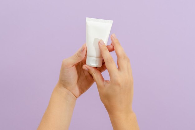 Tubo de crema cosmética en mano de mujer sobre fondo lila Concepto de belleza Tubo de embalaje para productos cosméticosxA