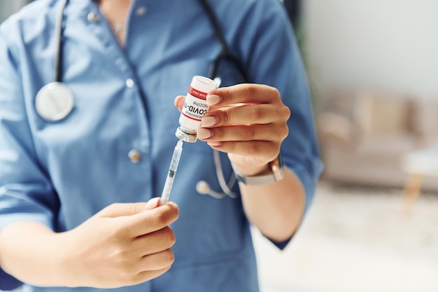 Tubo de ensaio com vacina Jovem médica de uniforme está dentro de casa