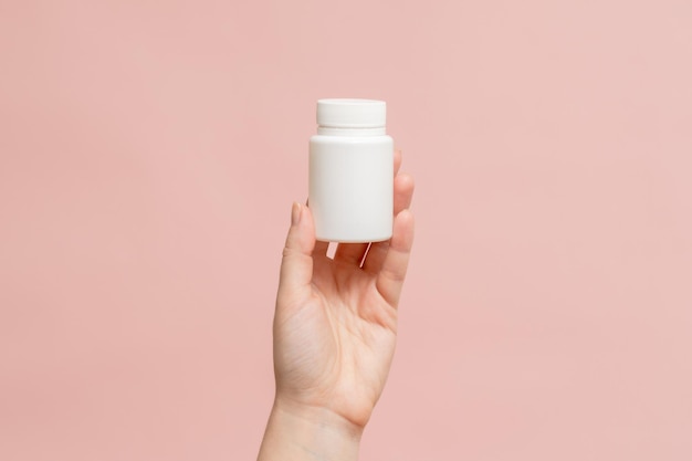Tubo de frasco de plástico na mão sobre um fundo rosa Embalagem para vitaminas, comprimidos, cápsulas ou suplementos