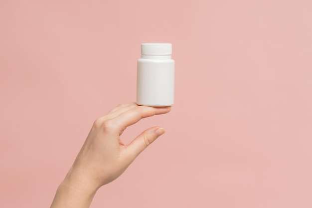 Tubo de garrafa de plástico na mão em um fundo rosa Embalagem para comprimidos de vitaminas ou cápsula ou suplemento