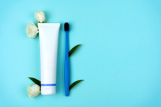Tubo de pasta de dentes de plástico reciclado com escova de dentes com flores brancas e folhagem em um fundo azul claro. Conceito de frescor e higiene. Consumo consciente. Copie o espaço