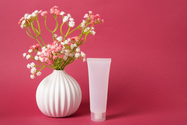 Tubo de plástico branco maquete para creme ao lado de um vaso com flores em um fundo de cor magenta