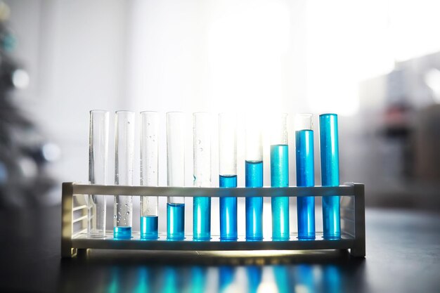 Tubo de ensayo con líquido azul en la mesa de laboratorio Examen de líquido bajo un microscopio