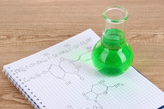 Foto tubo de ensayo con líquido colorido y fórmulas en la mesa