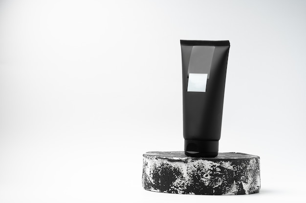 Tubo negro sin marca de producto cosmético en pedestal o podio blanco y negro sobre fondo blanco. Loción o crema para el cuidado de la piel en una pantalla de moda Foto horizontal Lugar para texto