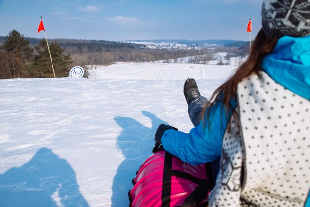 Tubo de nieve de niña desde la colina detrás de la actividad invernal