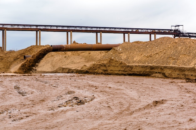 Foto tubo oxidado en la orilla del río, desde el cual fluyen las aguas residuales, lechada de arena sucia