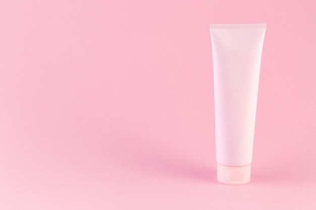 Tubo de plástico con crema facial o corporal sobre fondo rosa pastel con espacio de copia.