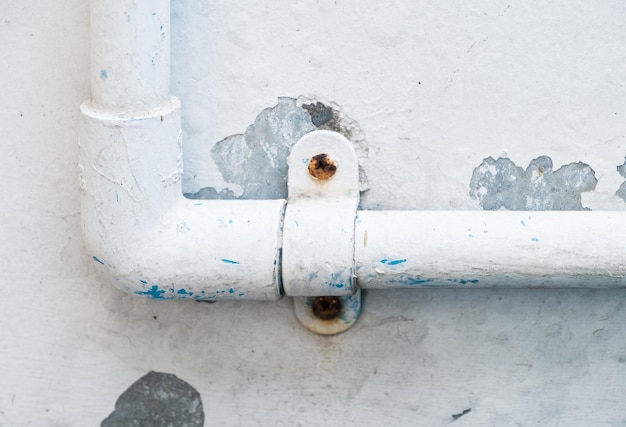 El tubo de PVC con la abrazadera de plástico para el sistema de suministro de agua en la casa urbana cerca del muro de hormigón blanco, vista frontal para el espacio de la copia.