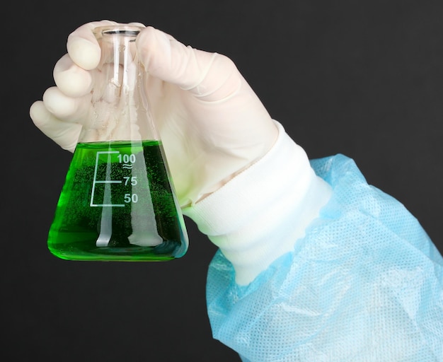 Tubo de vidrio con líquido en la mano del científico durante la prueba médica sobre fondo negro