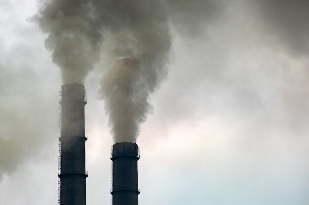 Tubos altos da usina de carvão com fumaça preta subindo para a atmosfera poluente.