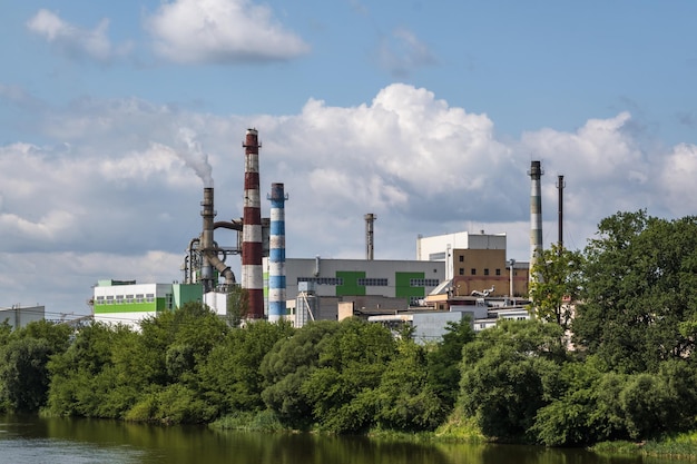 Tubos de serraria de fábrica de marcenaria perto do rio Conceito de poluição do ar Paisagem industrial poluição ambiental resíduos de usina termelétrica